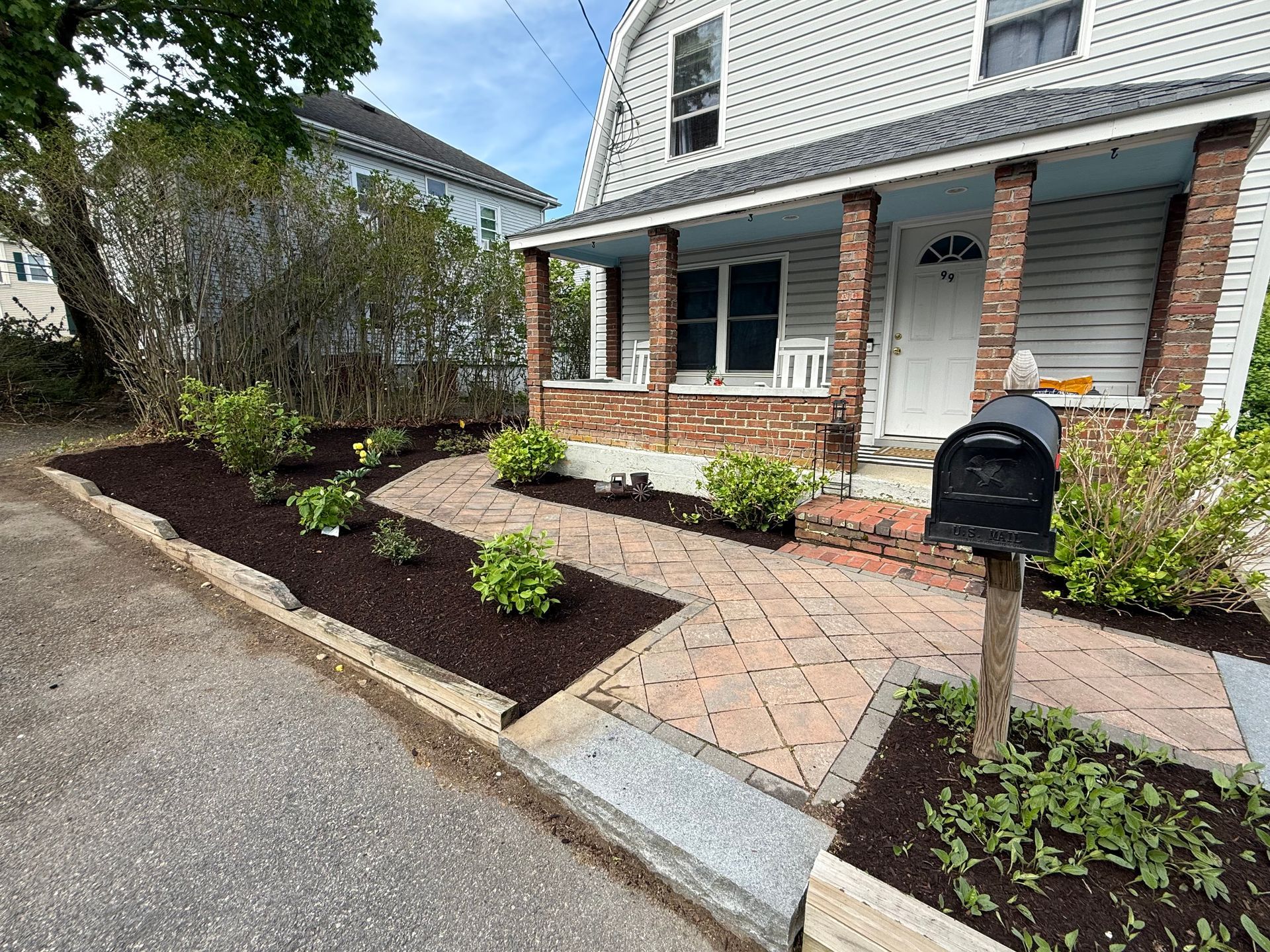 Front yard garden beds along a brick walkway beside a house and mailbox