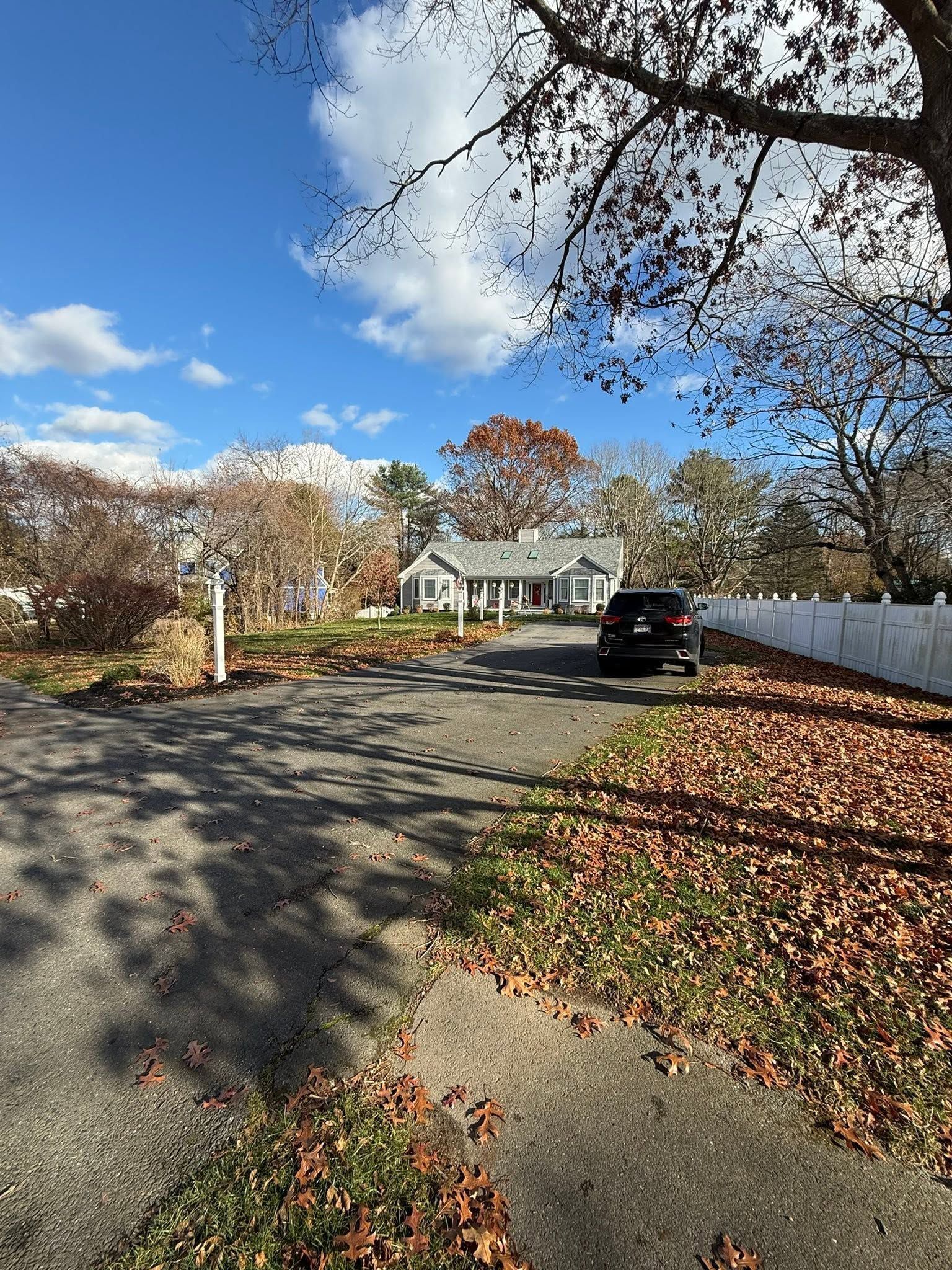 Quiet suburban street lined with autumn leaves, blue sky, houses, and a parked black SUV.