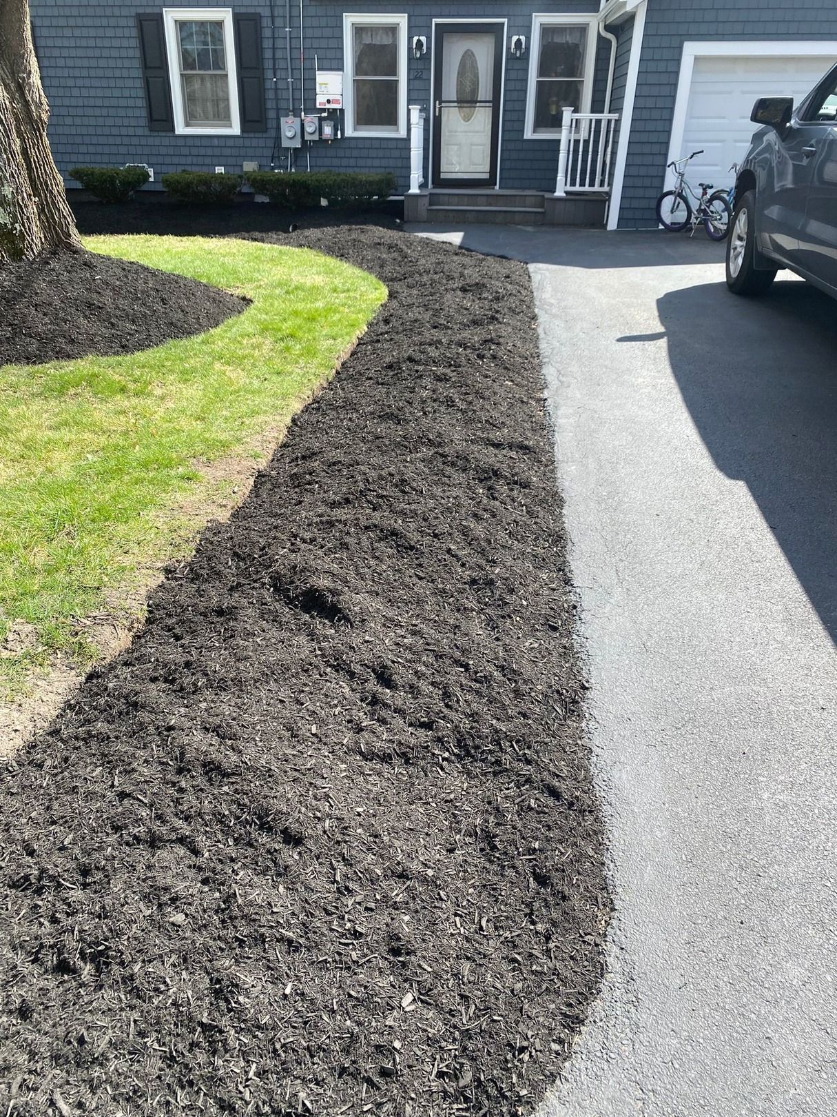 Fresh mulch bed bordering a driveway and green lawn in front of a house