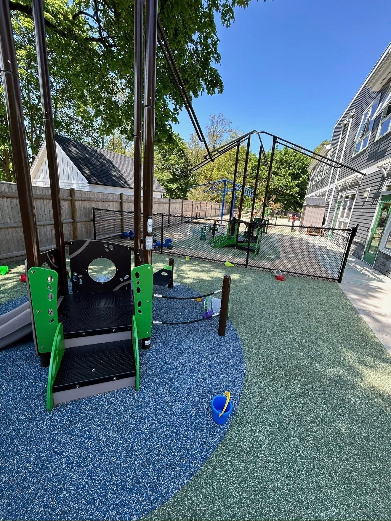 Outdoor playground with climbing structure, slides, and a netted play area under trees.