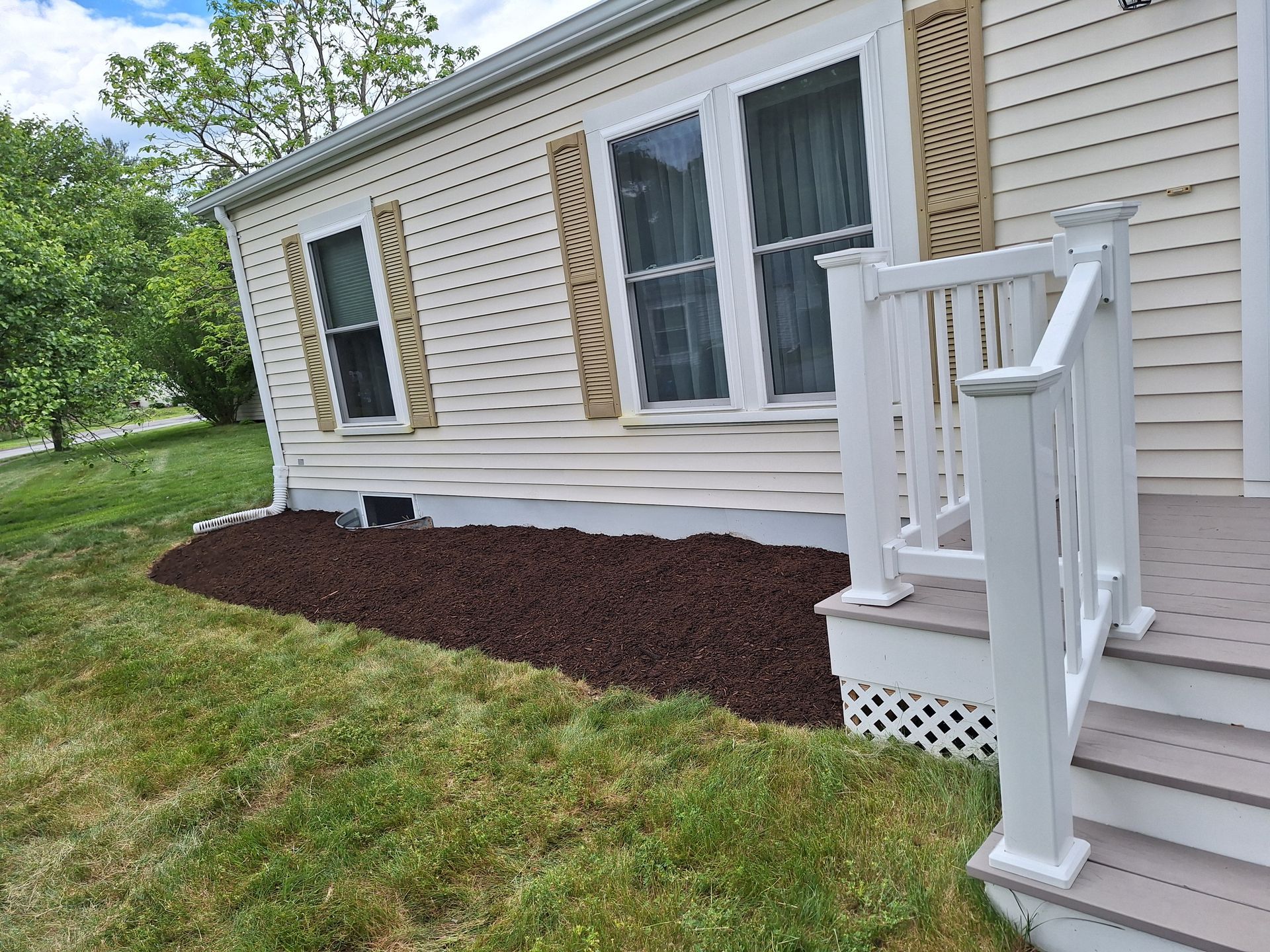 Side of a beige house with white porch steps and fresh brown mulch along the foundation.
