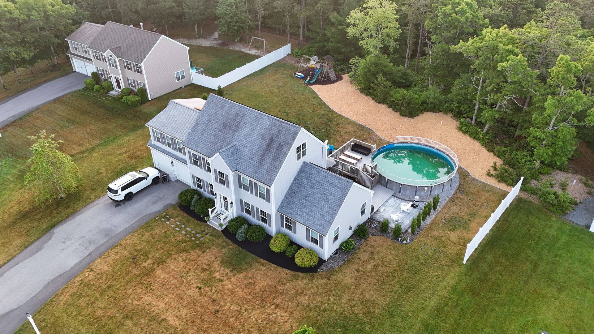 Aerial view of a gray house with a driveway, lawn, and backyard pool surrounded by trees.
