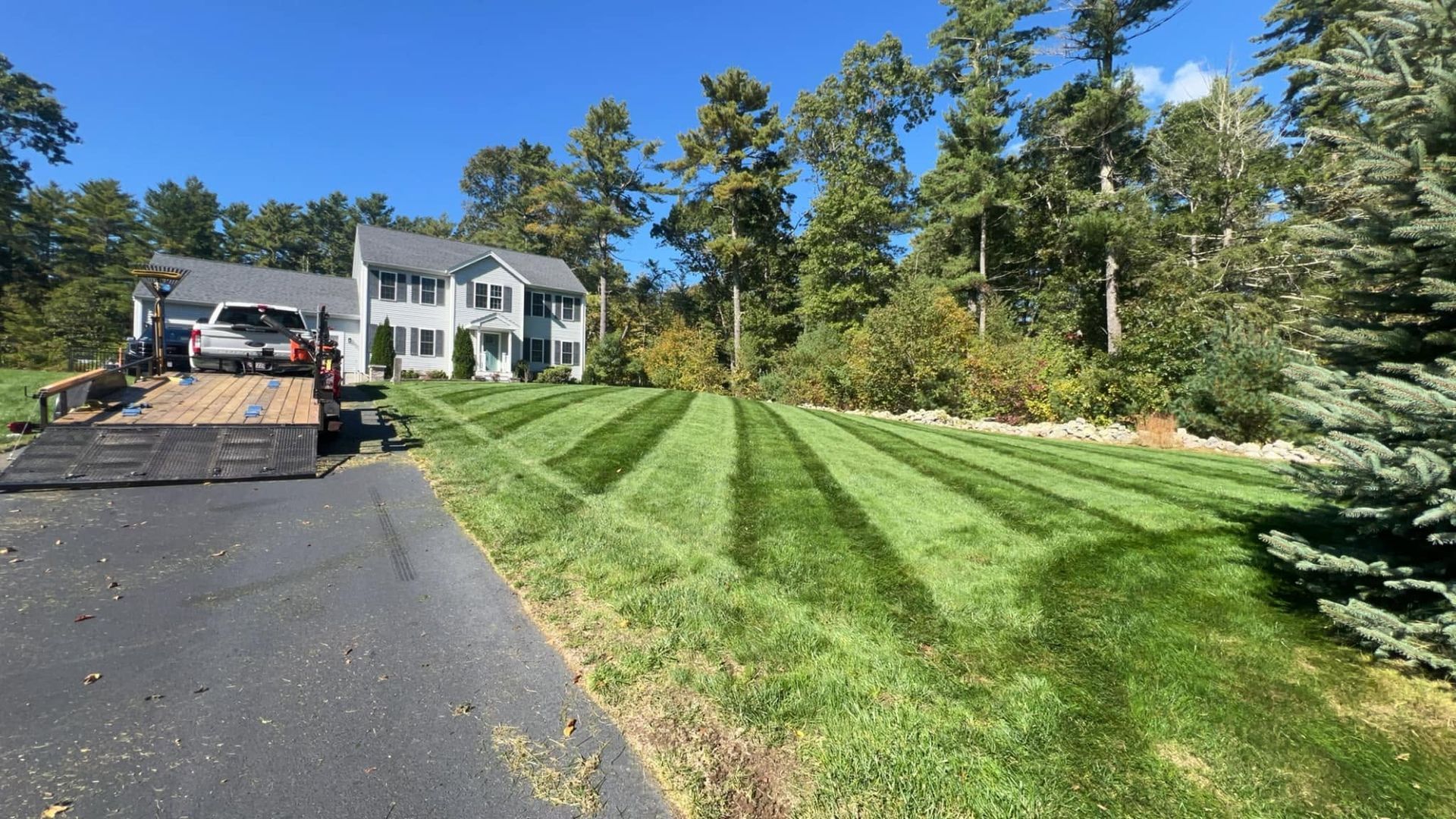 House with freshly striped green lawn beside a paved driveway and wooded yard