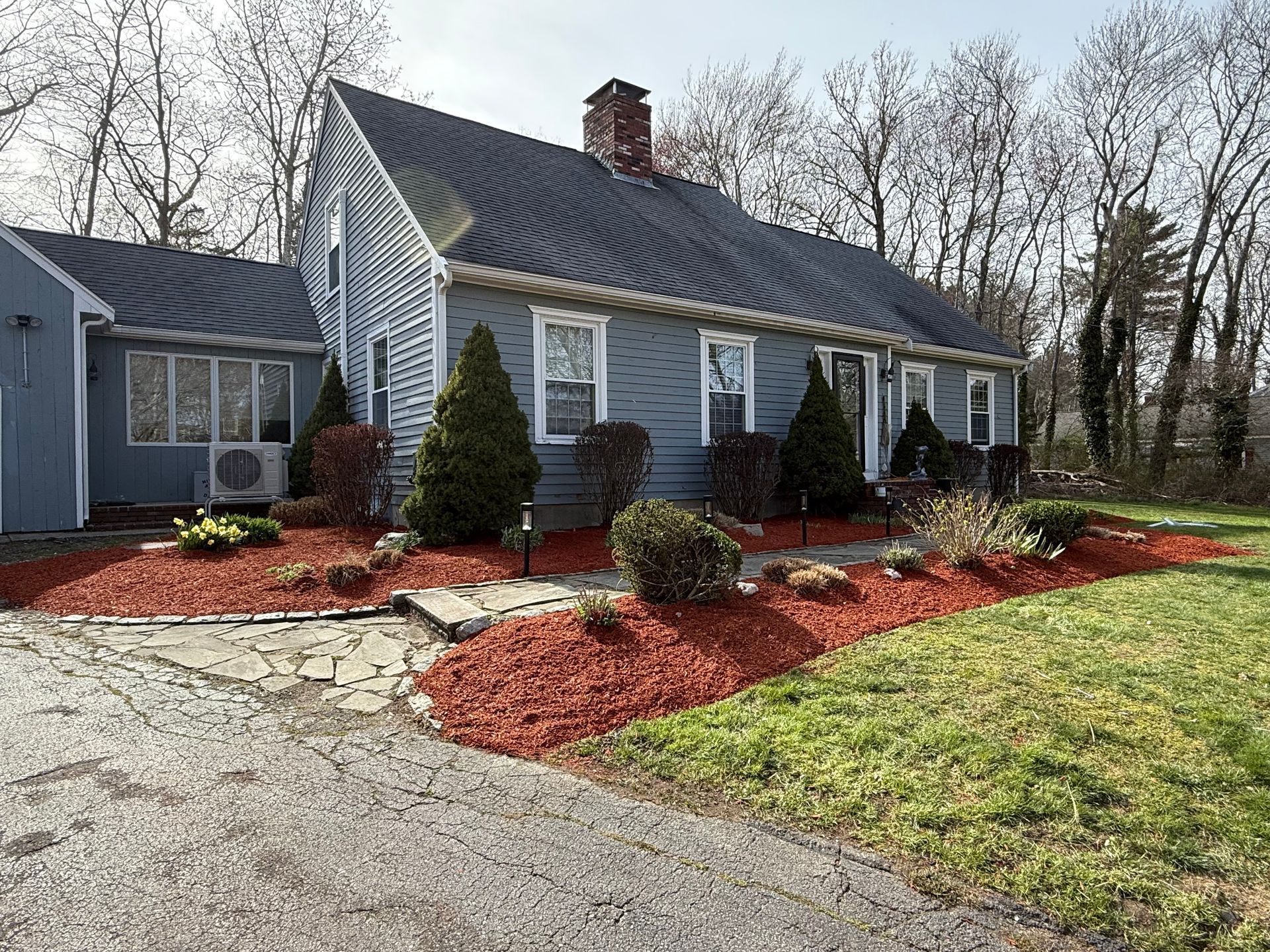 Blue house with white trim, stone walkway, and red mulch landscaping in a wooded yard