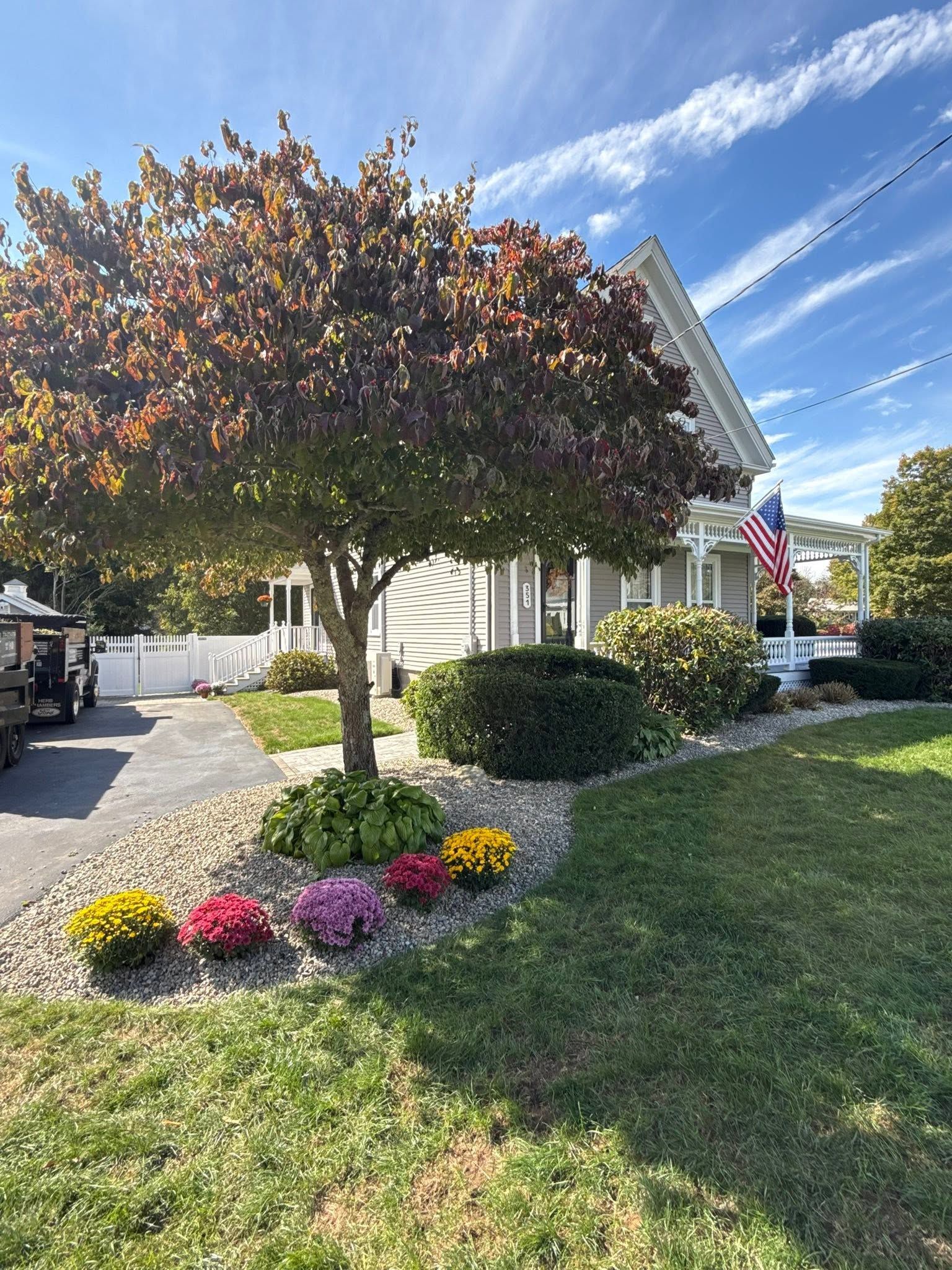 Landscaped house with a flowering tree, colorful flower bed, lawn, and an American flag by the porch.