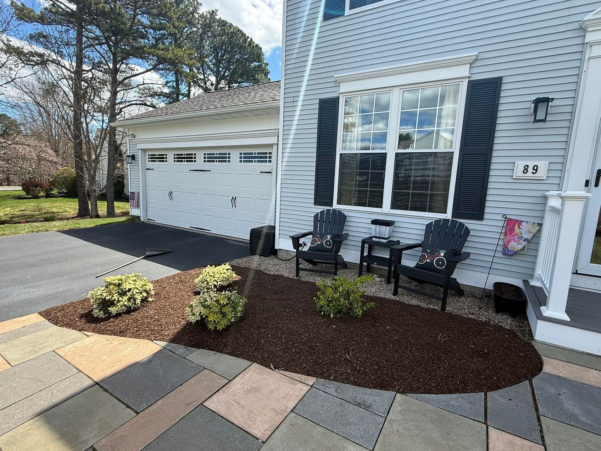 Front porch of a blue house with black shutters, garage, potted chairs, and a landscaped walkway.