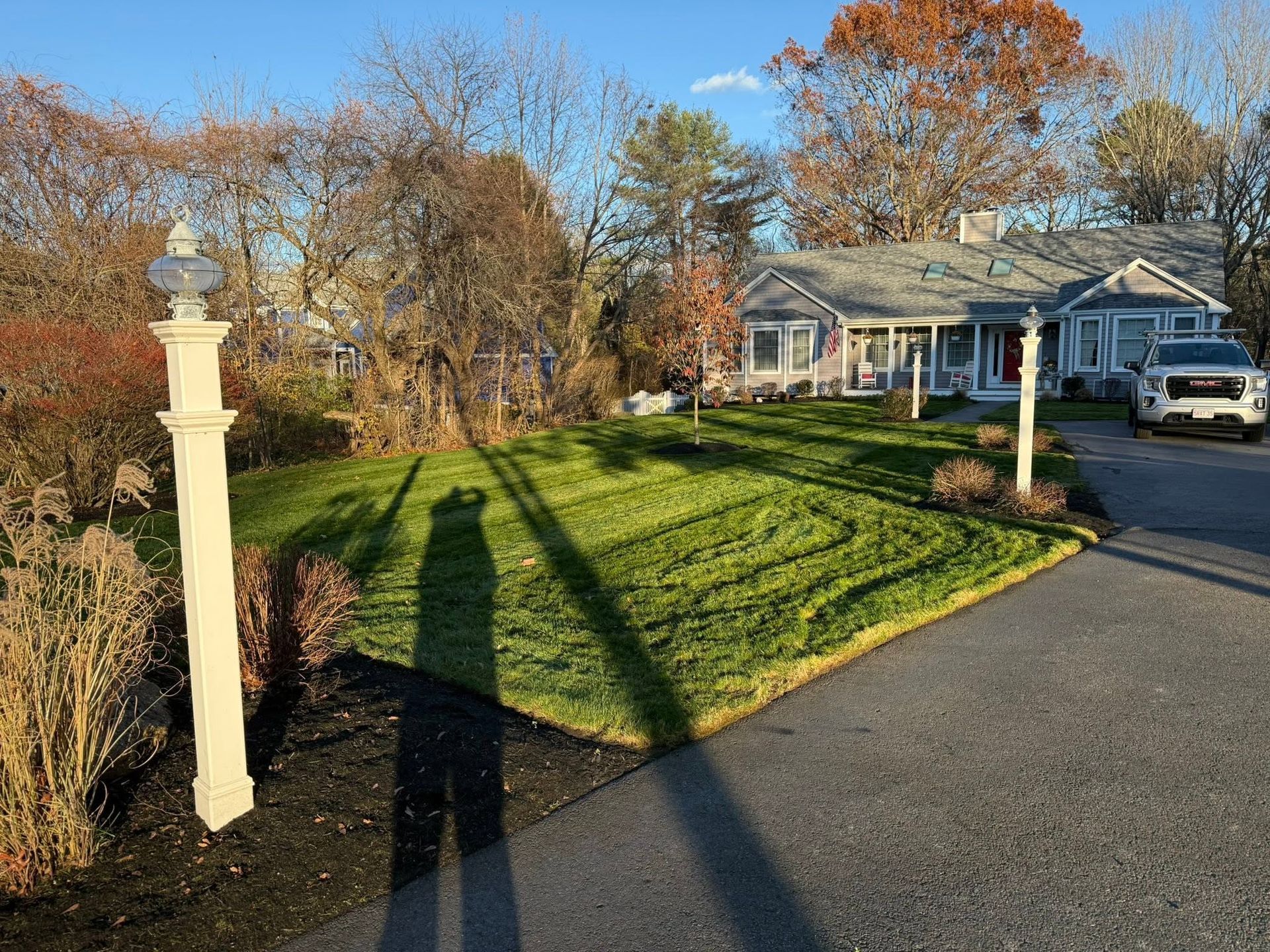 Suburban front yard with green lawn, long shadows, driveway, and a house in autumn sunlight