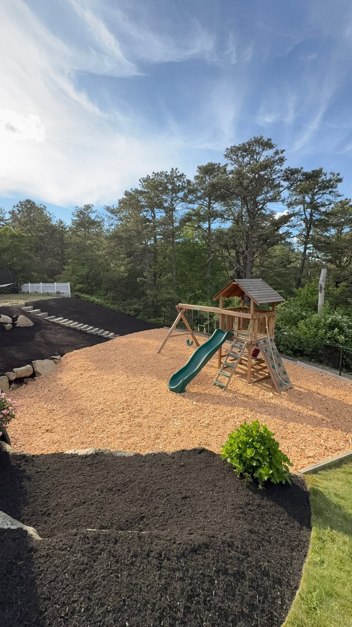 Outdoor playground with a wooden playset, green slide, and wood-chip ground under a blue sky.