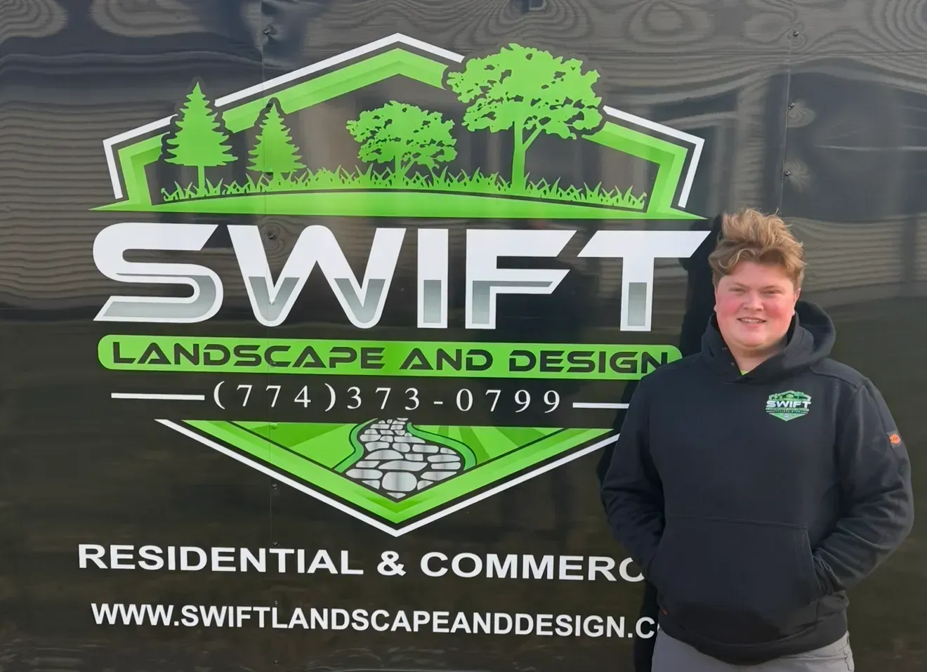 Person standing beside a Swift Landscape and Design sign outdoors