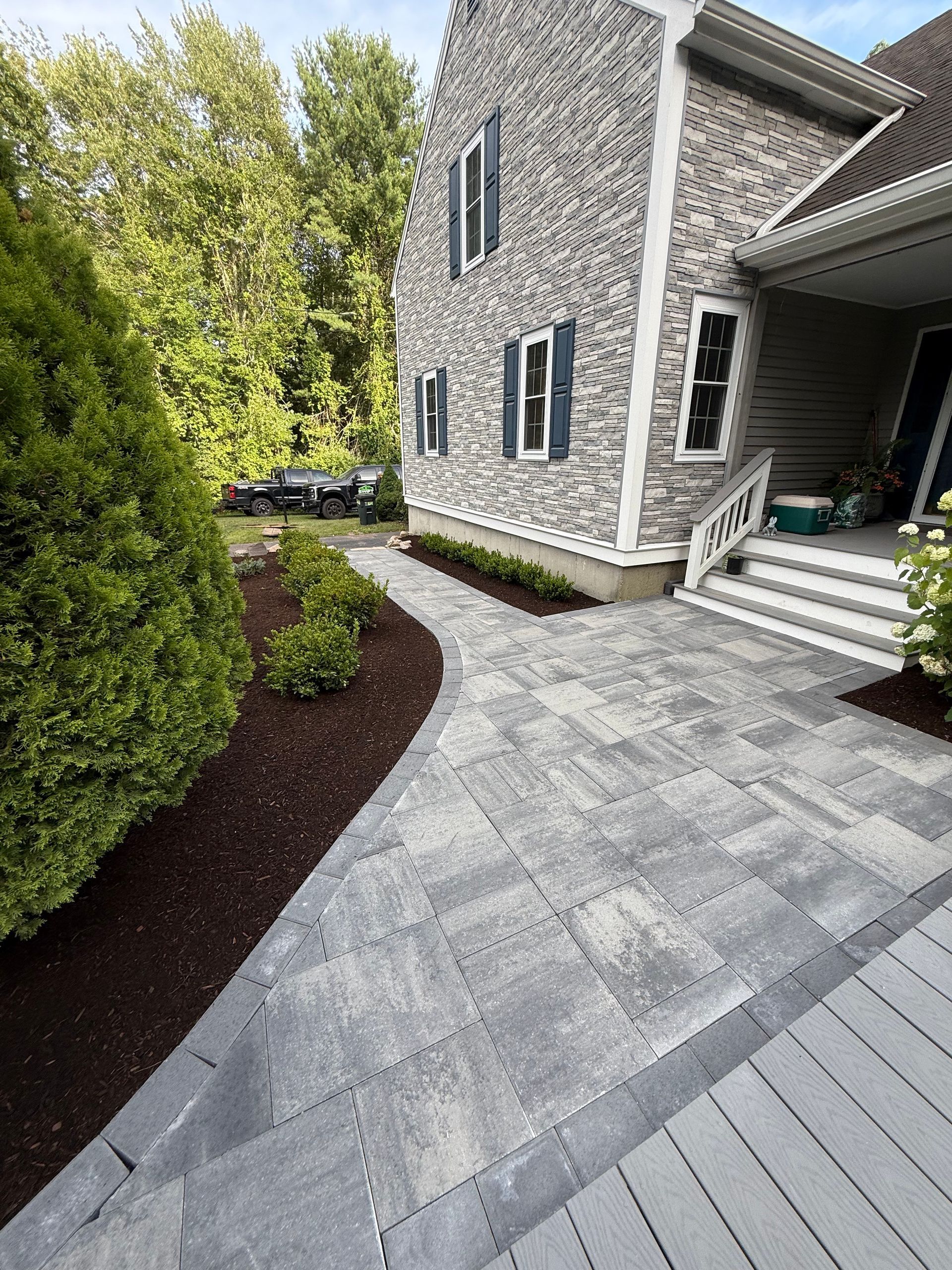 Red roses line a porch beside a green lawn with stepping stones and trees.