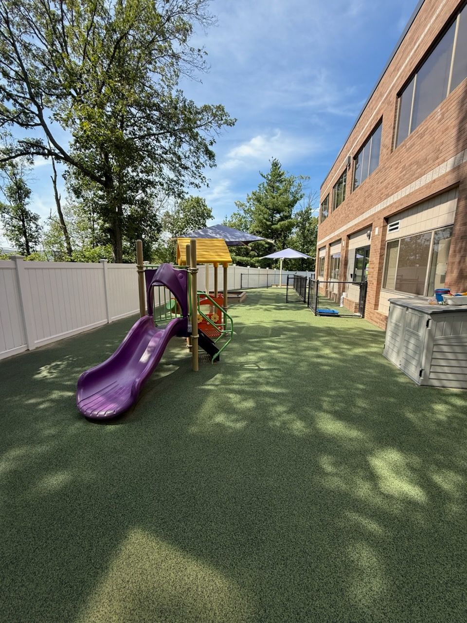Wooden playground set with slides on a mulch pad in a grassy backyard, surrounded by trees.