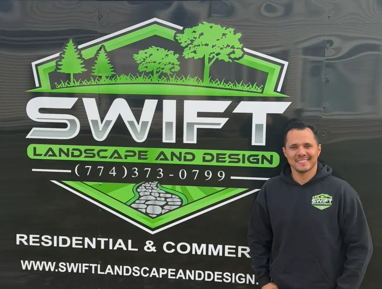 Swift Landscape and Design sign with green logo; man in black hoodie stands at right.