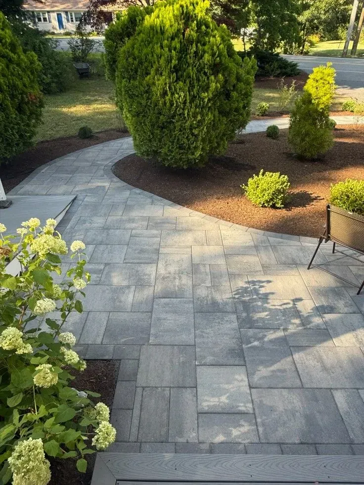 Curved gray stone patio path beside landscaped garden with shrubs and trees