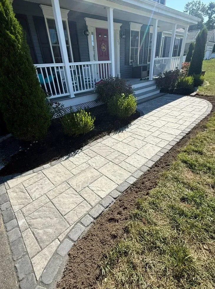 Curved stone walkway leading to a front porch with white railing and shrubs beside a house