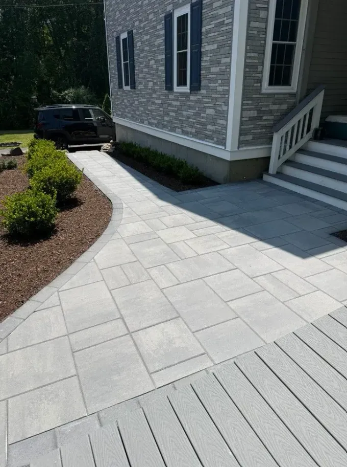 Stone walkway beside a house, leading past steps to a driveway with a parked black car.