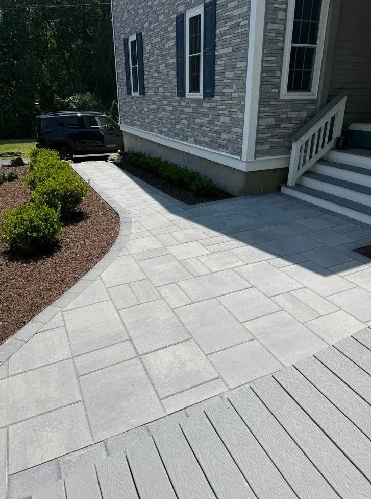 Stone walkway and front entry of a house with gray siding, steps, and landscaped shrubs