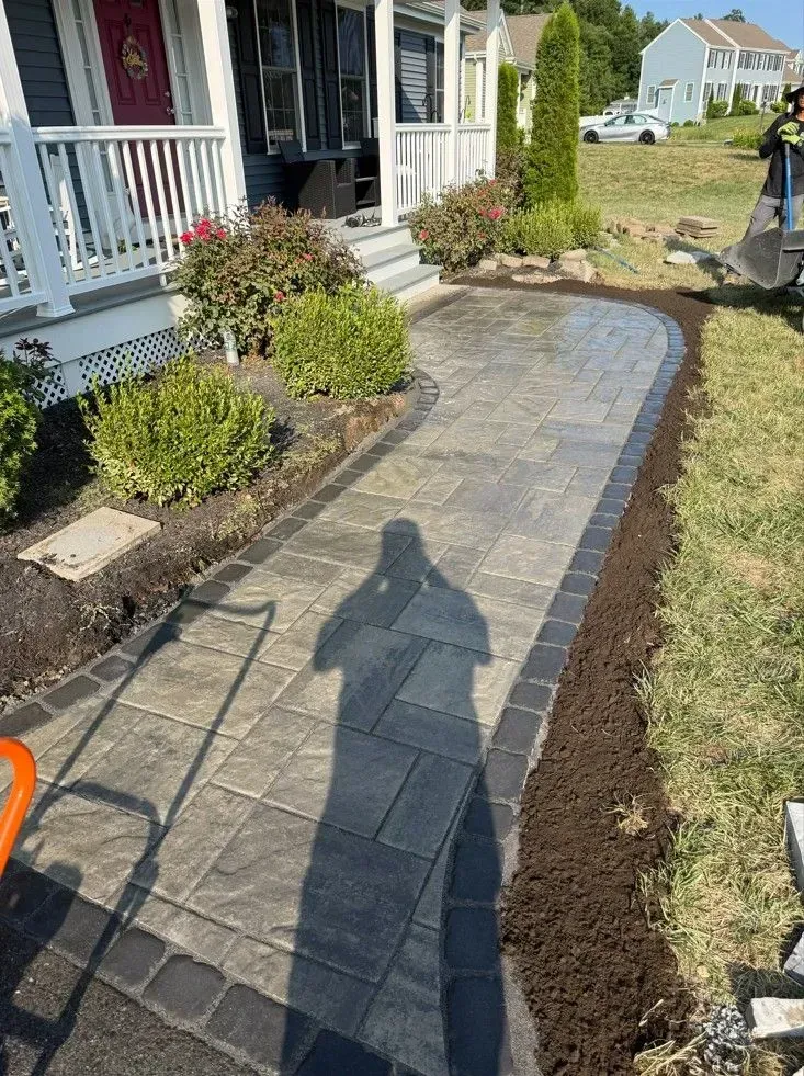 Brick walkway under construction beside a house, with fresh edging and a shadow of the photographer.