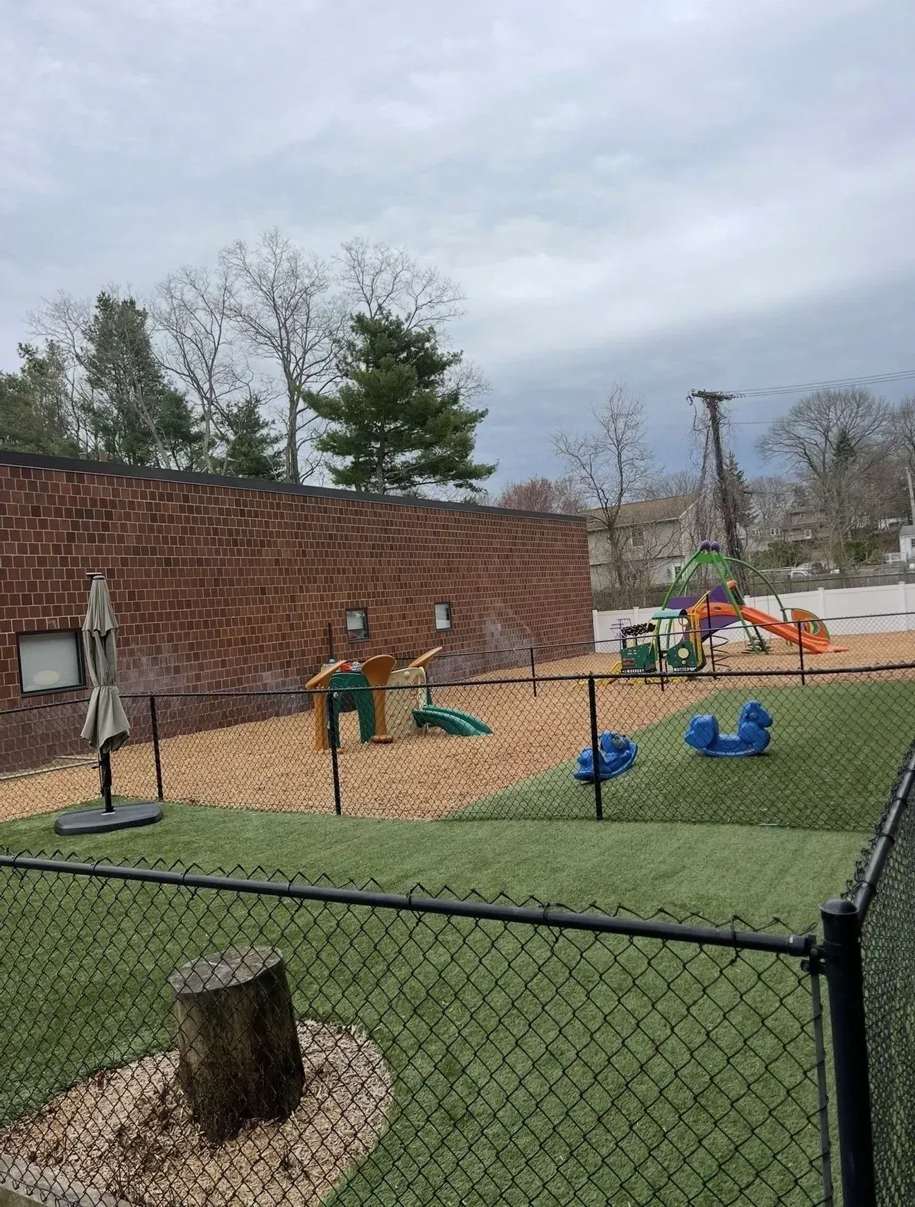 Playground with tan mulch, black borders, a wooden playset and green slide under a blue sky, surrounded by trees