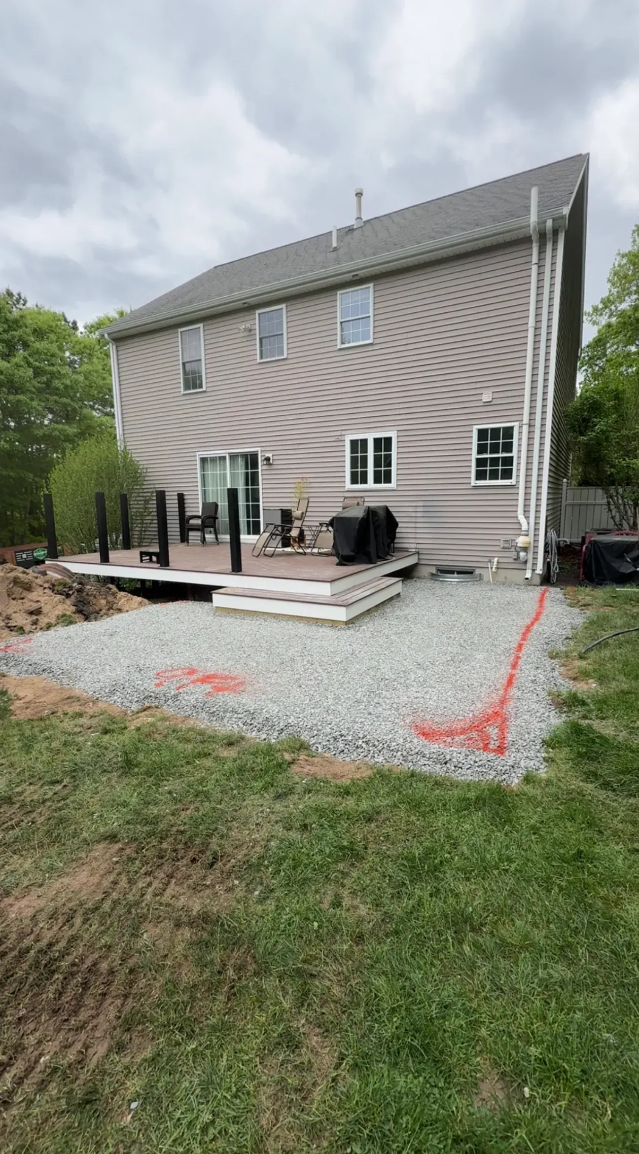 Backyard view of a beige house with a gravel patio, outdoor furniture, and a sloped green lawn