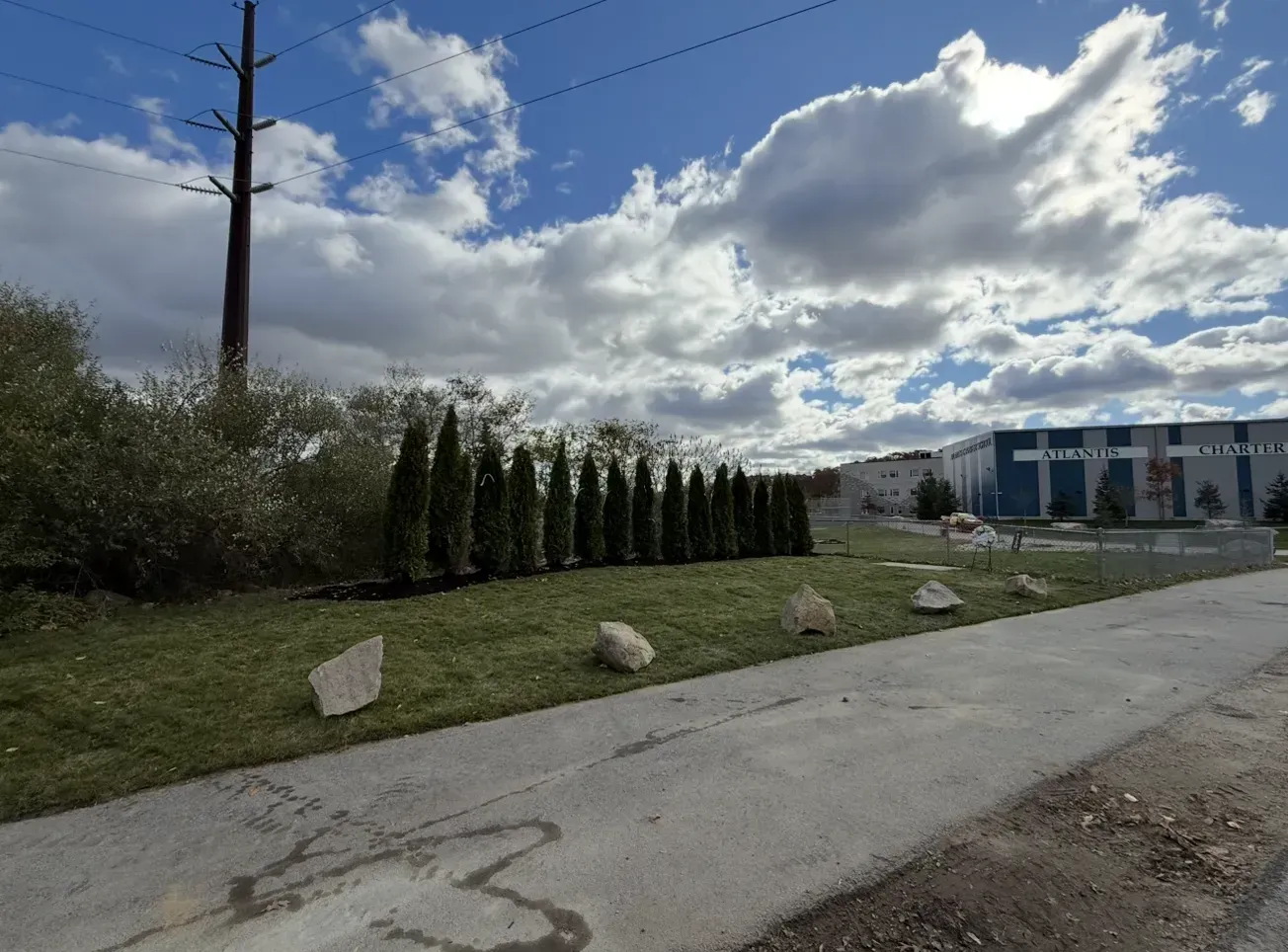 Cloudy roadside with trimmed hedges, a grassy verge, and a building in the distance