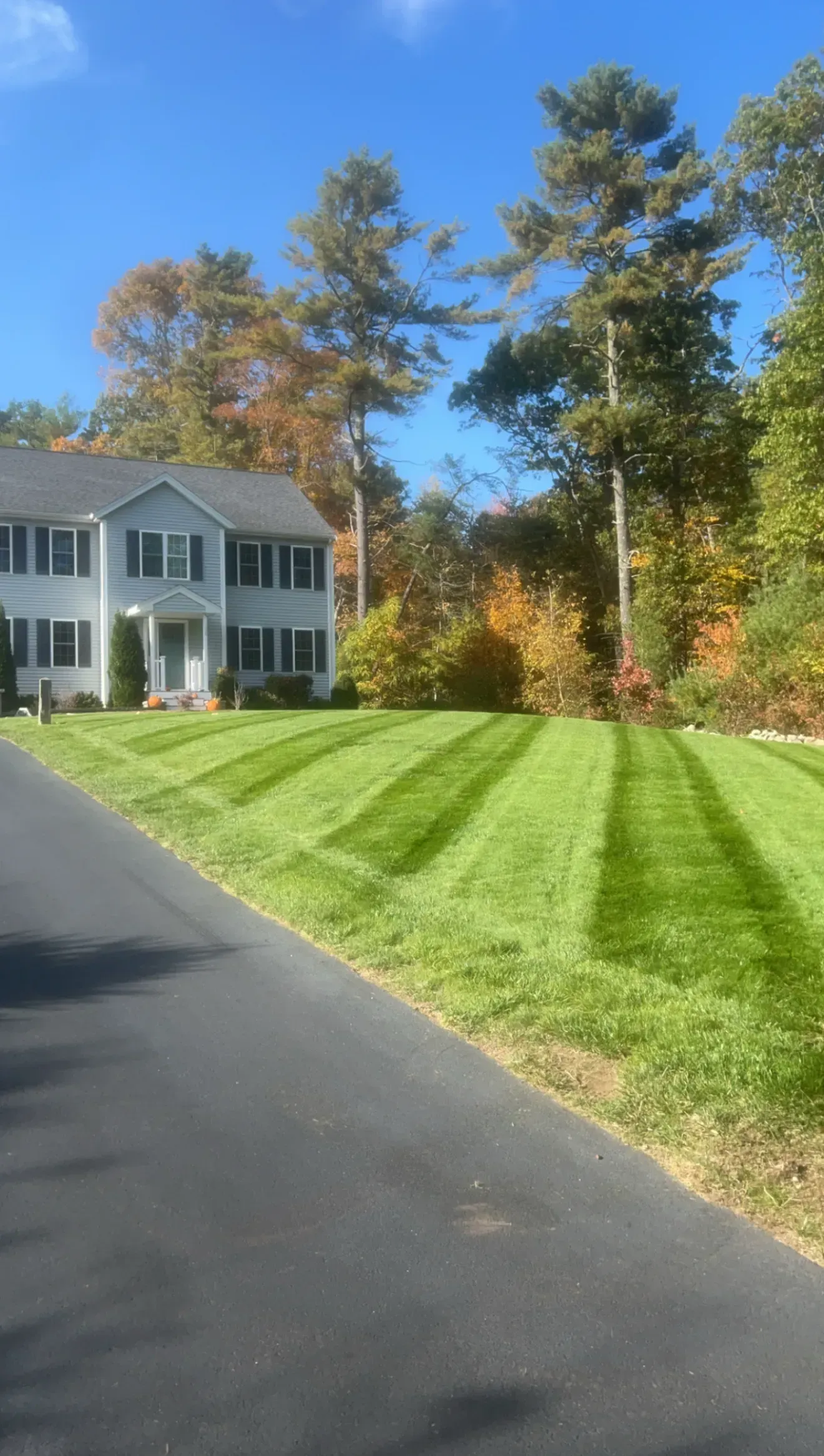 White house beside a freshly mowed lawn and paved driveway under a sunny autumn sky