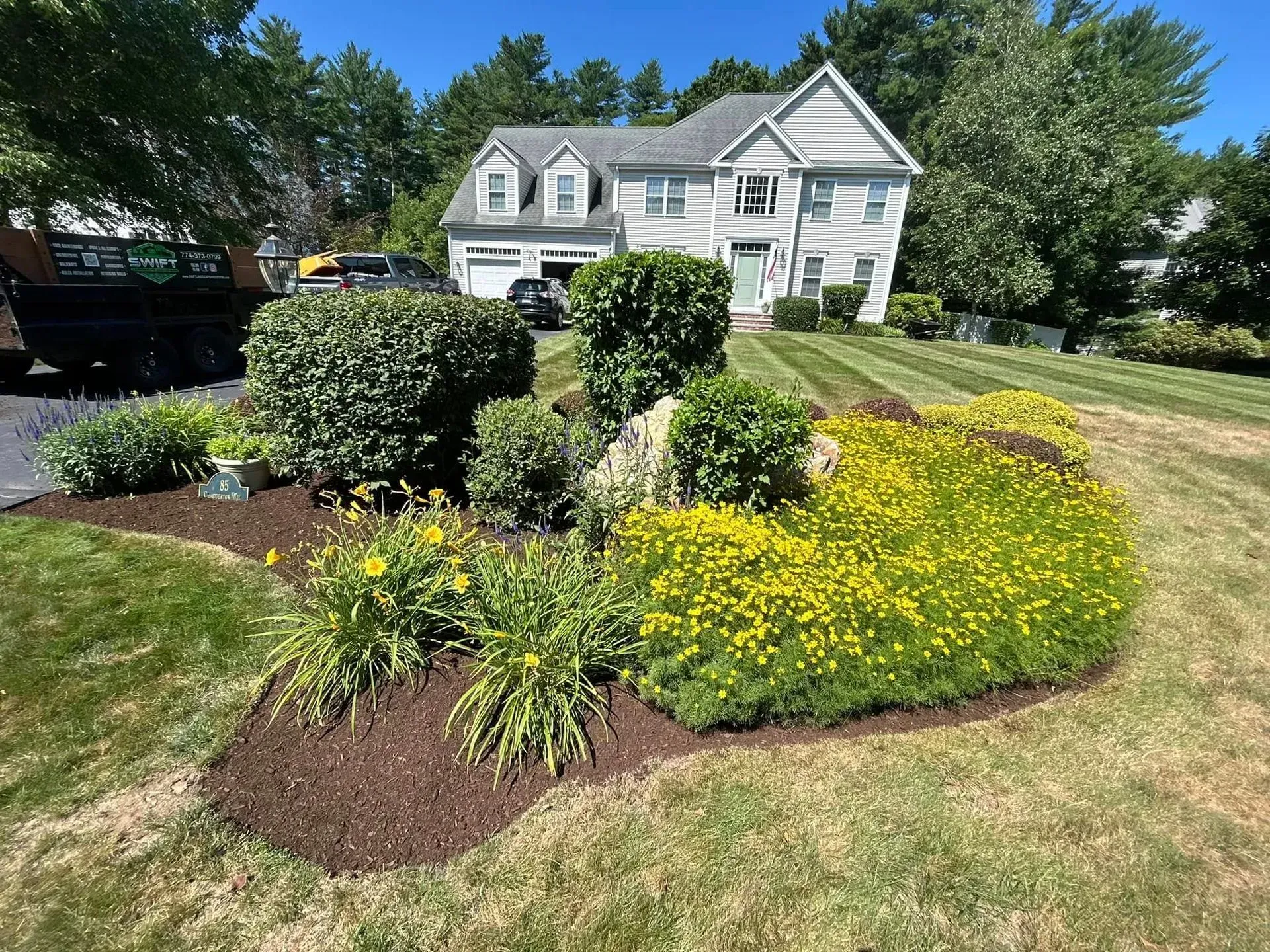 White house with a landscaped front yard, shrubs, and yellow flowers along a curved lawn.