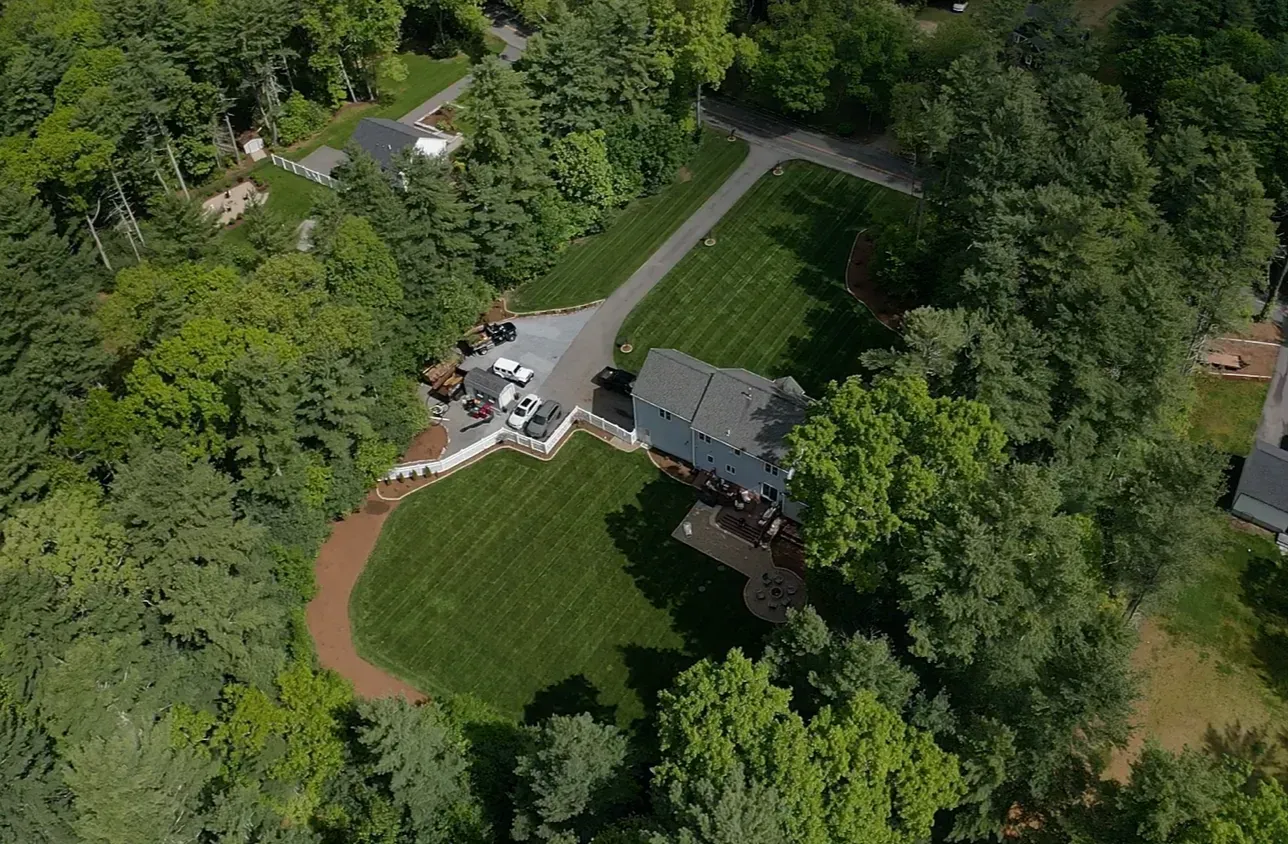 Aerial view of a house with a circular lawn, driveway, and surrounding trees in a wooded area