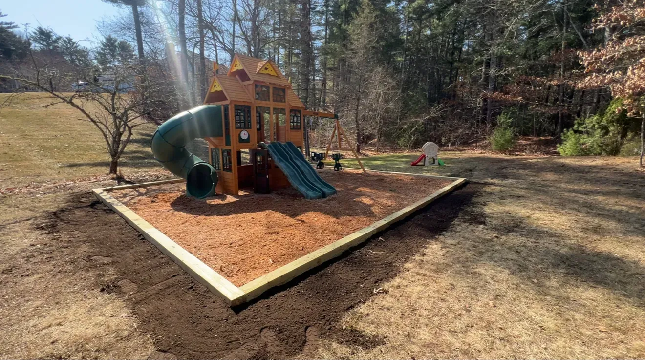 Children’s wooden playground with slides and a sandbox in a wooded yard