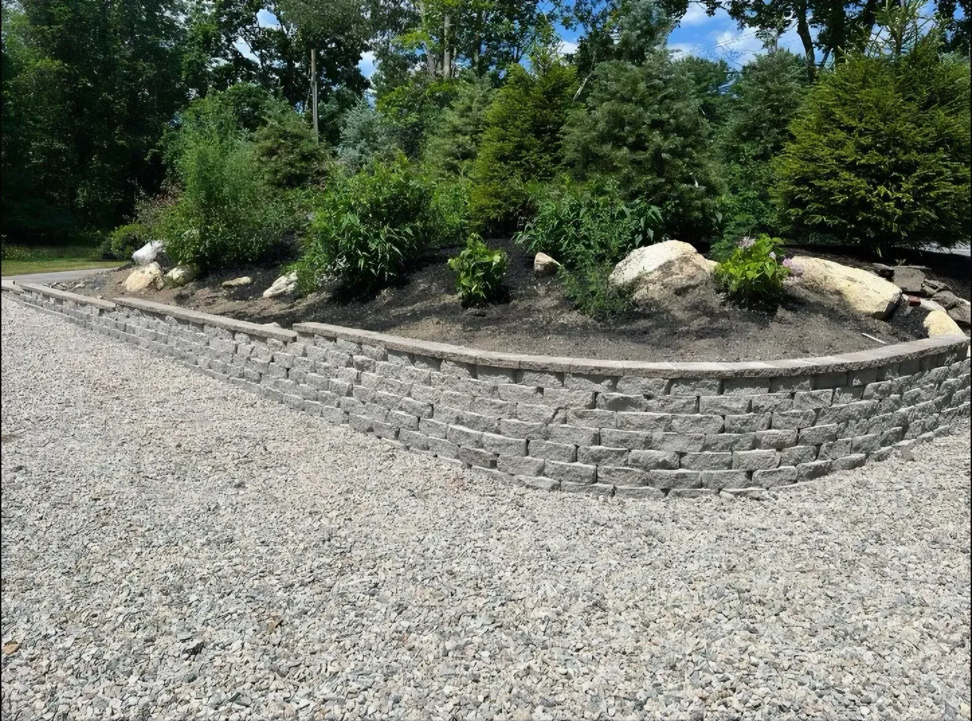 Brick walkway beside house with pink flowering shrubs and green bushes along the siding