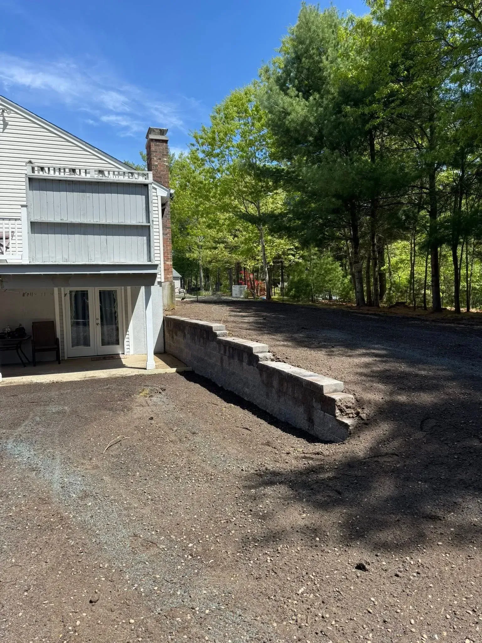 Backyard patio beside a white house, with gravel ground and trees in bright sunlight.