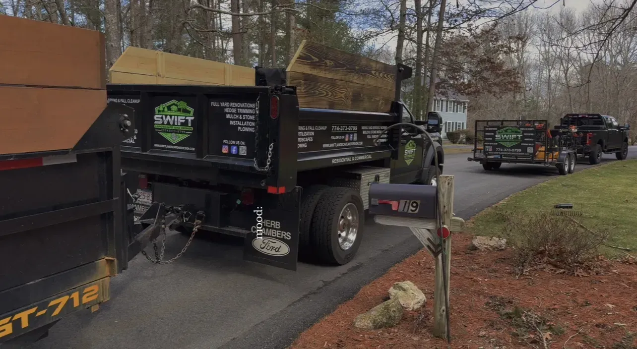 Dump truck and utility trucks parked along a roadside in a wooded area.