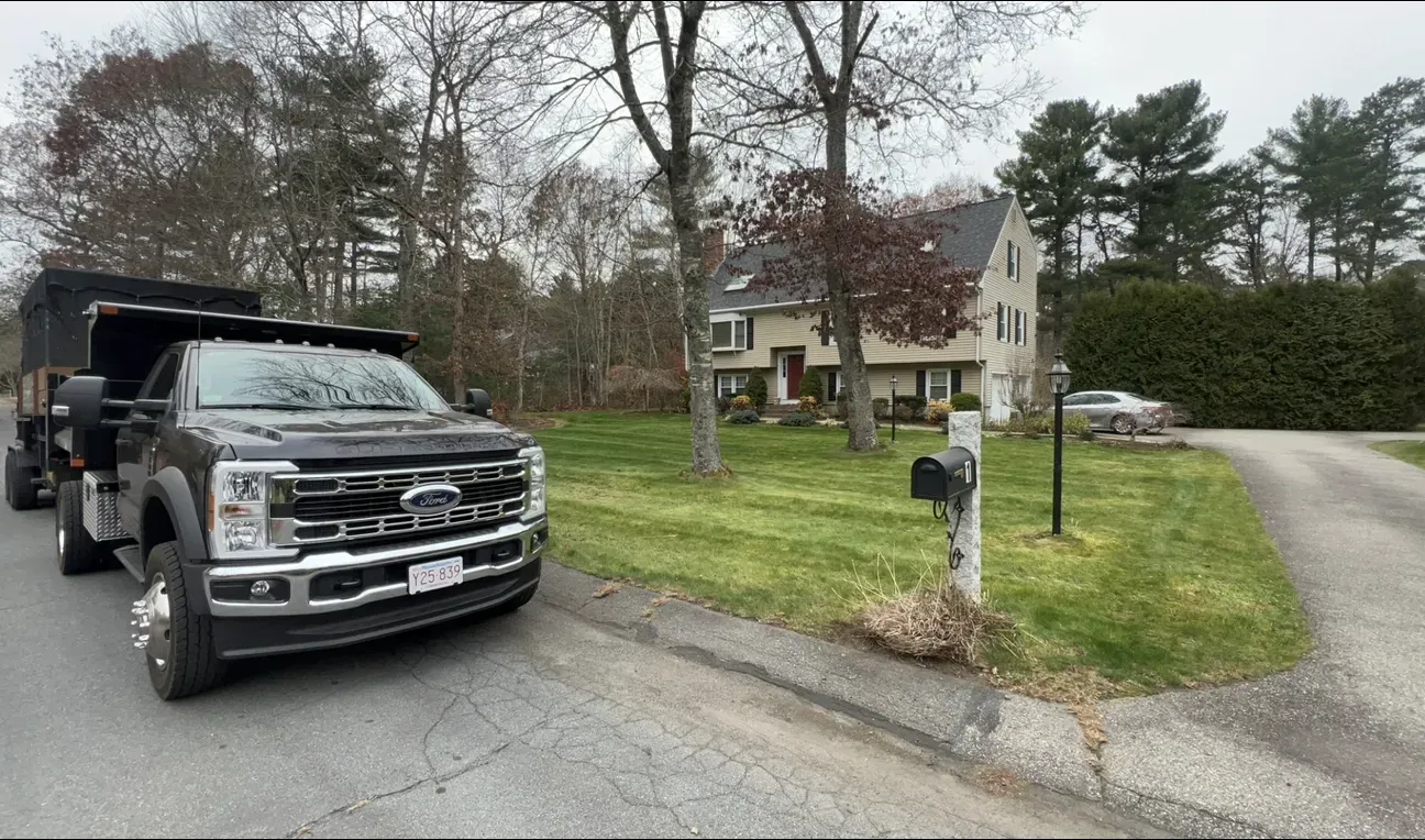 Black pickup truck parked by a mailbox beside a suburban house on a grassy corner lot.