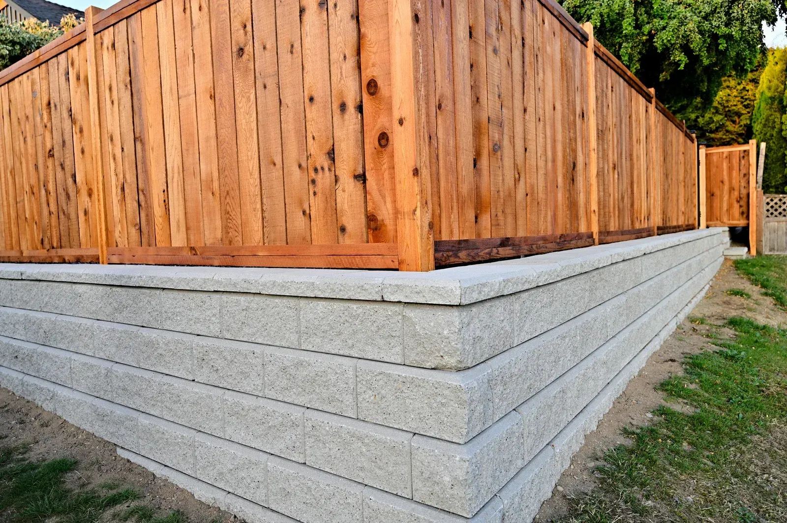Wooden fence atop a gray concrete retaining wall along a sloped yard