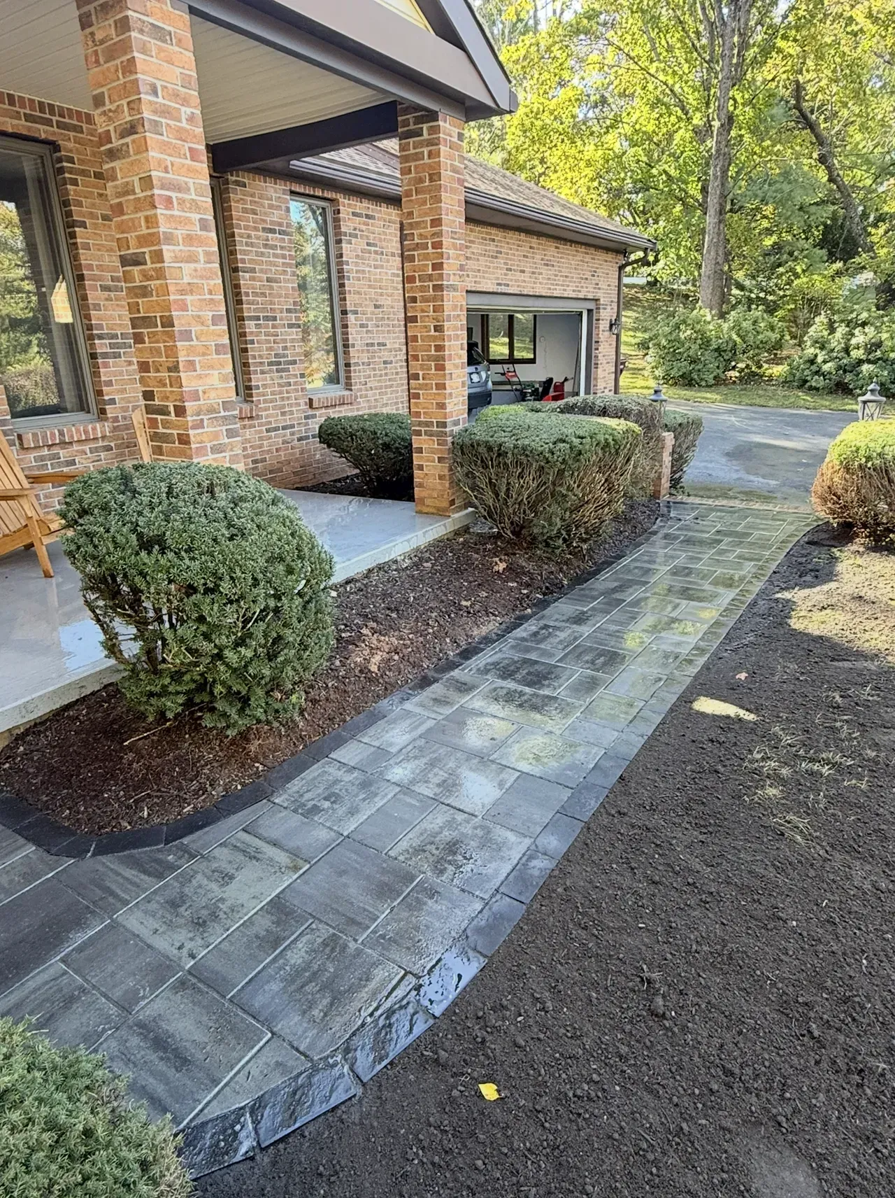 Brick house front walkway with gray pavers, shrubs, and a gravel driveway￼