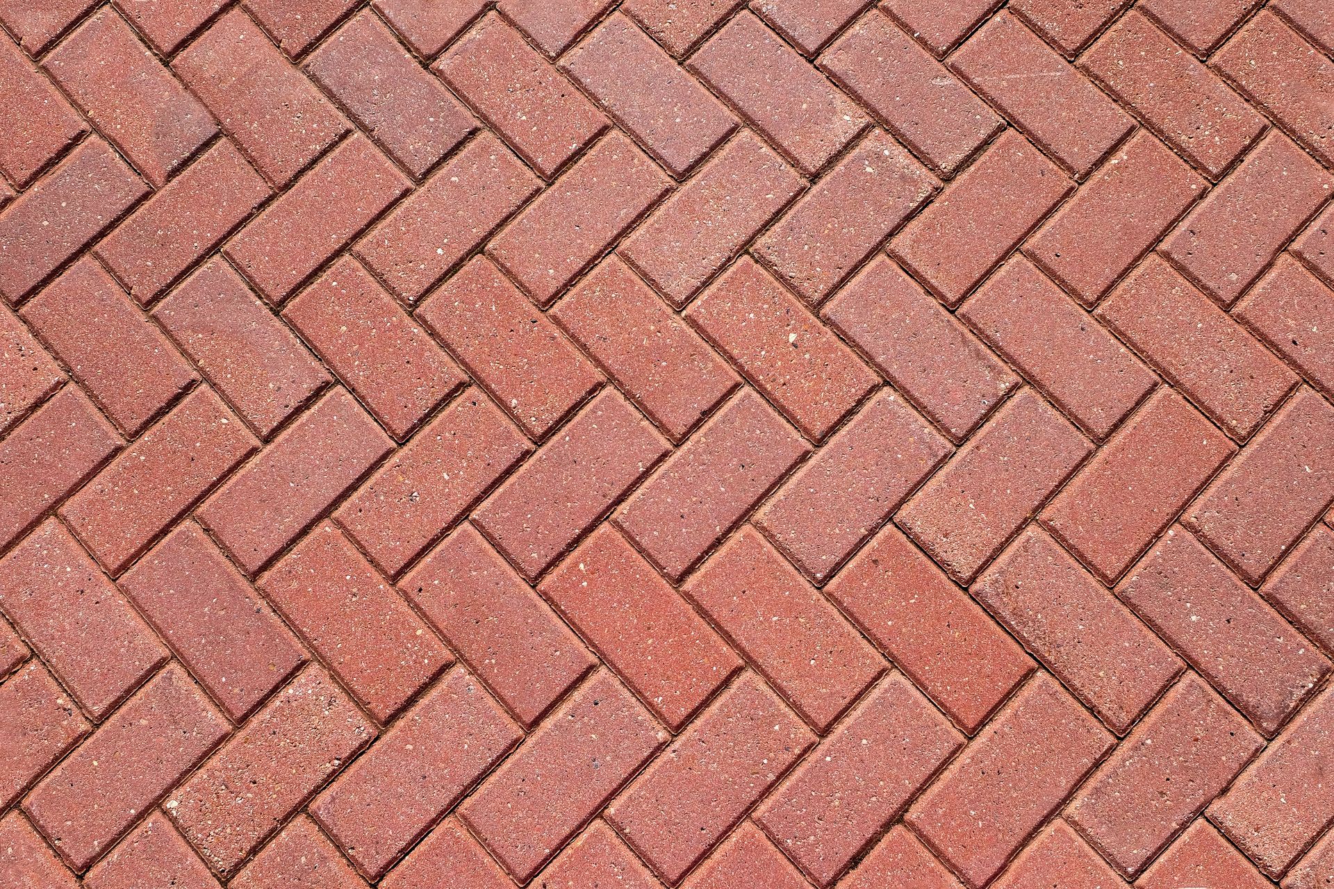 A close up of a red brick pavement in a herringbone pattern.