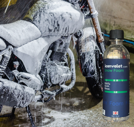 A motorcycle is covered in foam next to a bottle of snow foam