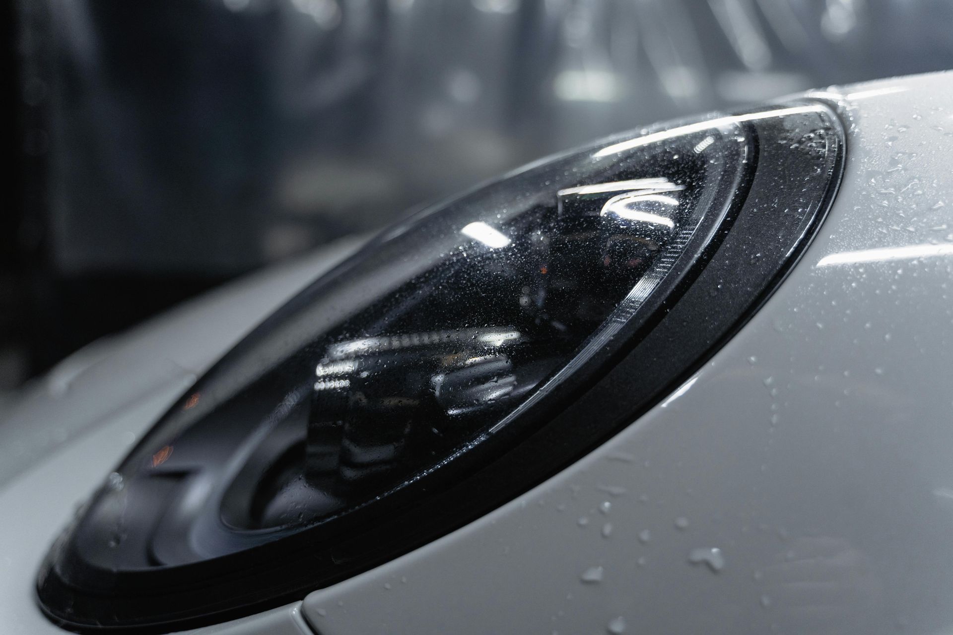 A close up of a car headlight with water drops on it.