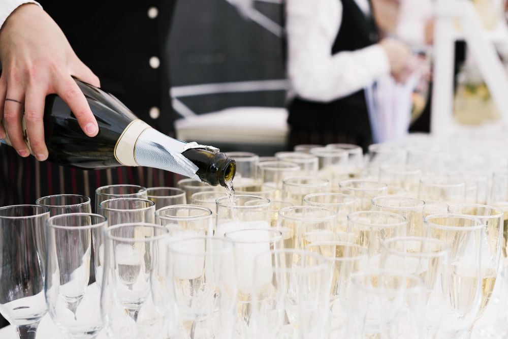 Um barman está servindo champanhe em uma fileira de taças.-Pousada-Recanto-do-Chef