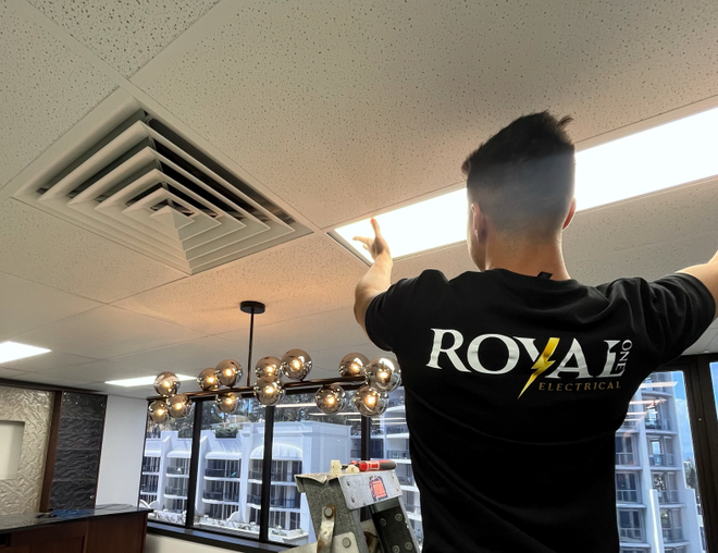 A man wearing a royal electrical shirt is working on a light fixture.