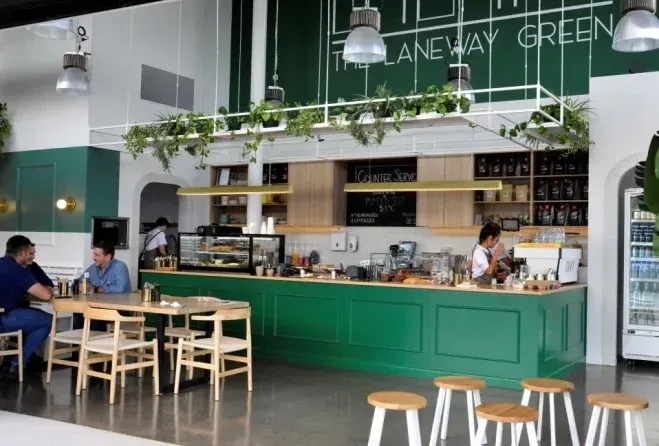 Two men are sitting at tables in a restaurant with a green counter.