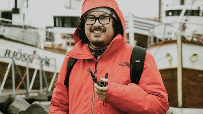 A man in a red jacket is standing in front of boats.