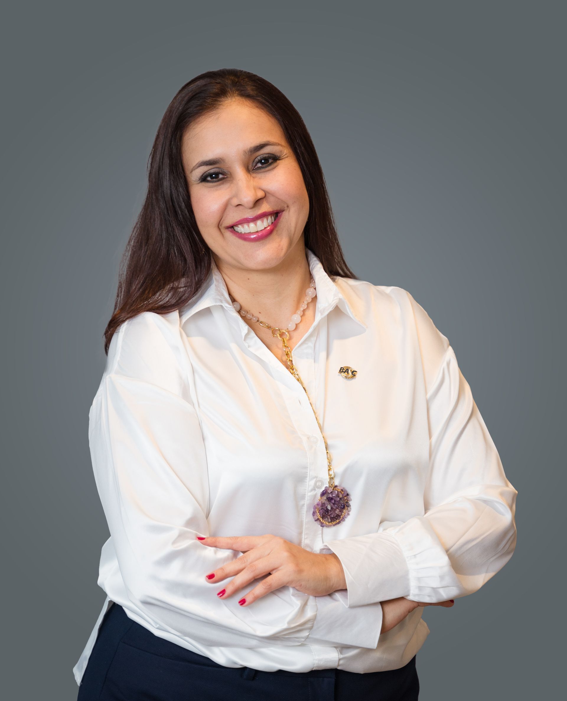 Una persona sonriente con cabello largo y oscuro viste una camisa blanca 