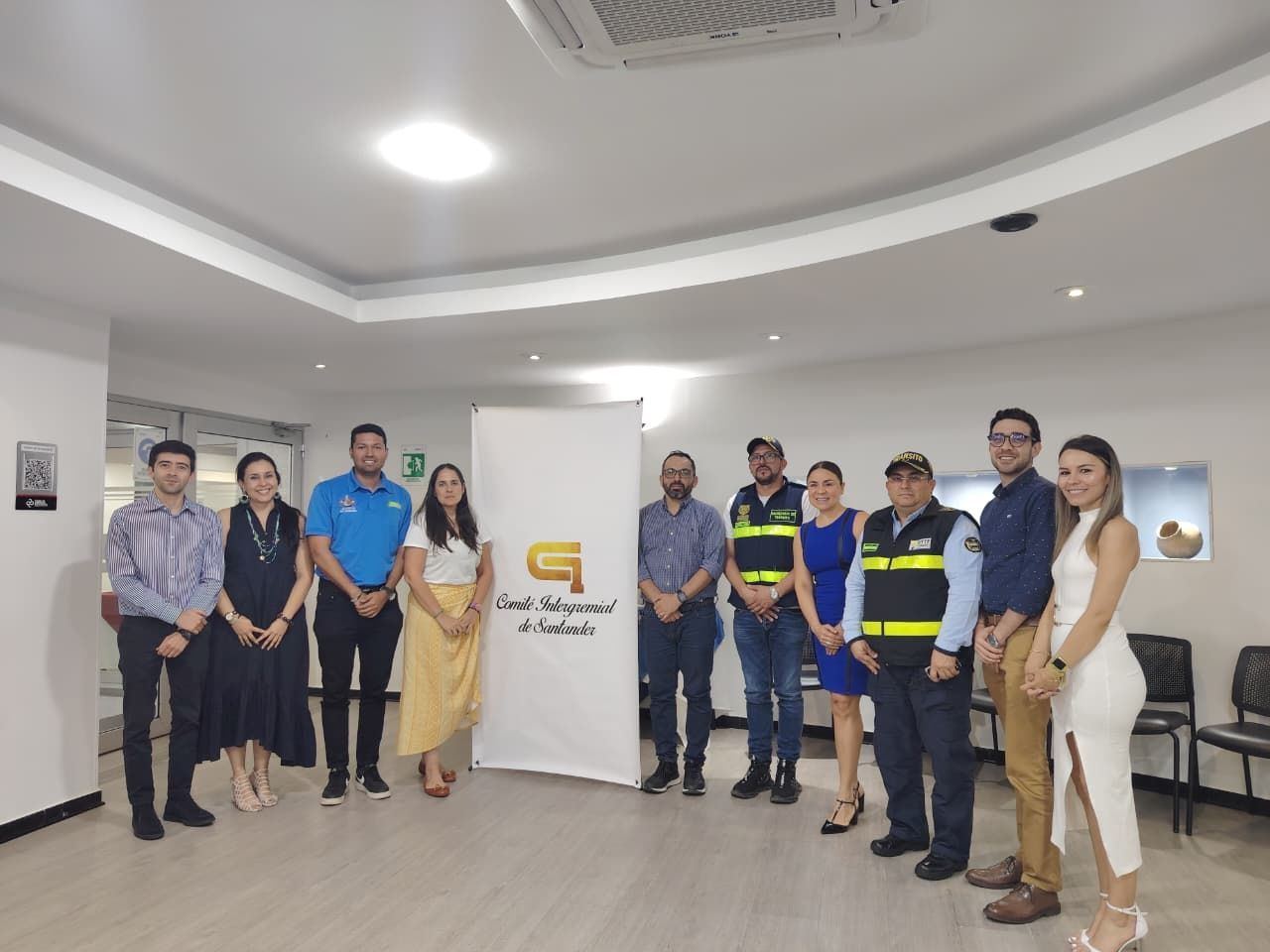 Un grupo de personas se encuentra en una oficina, frente a una pancarta blanca con un logotipo.