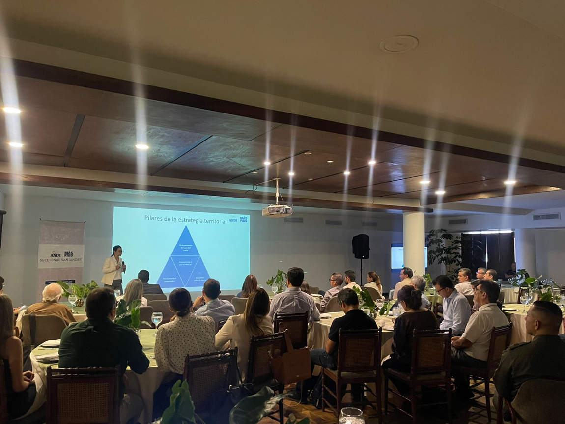 Un orador realiza una presentación frente a una pantalla de proyección ante un público sentado en una sala de conferencias.