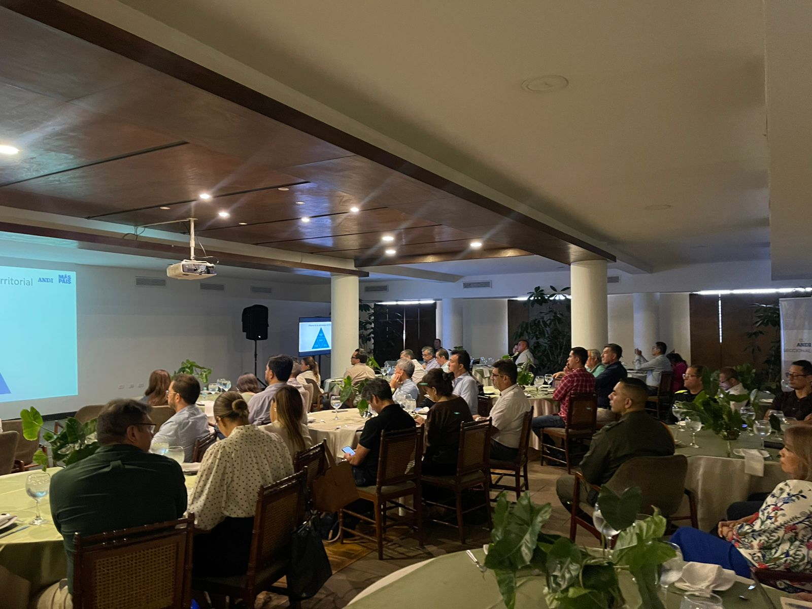 Un grupo de personas sentadas en mesas redondas en una sala de conferencias con poca luz