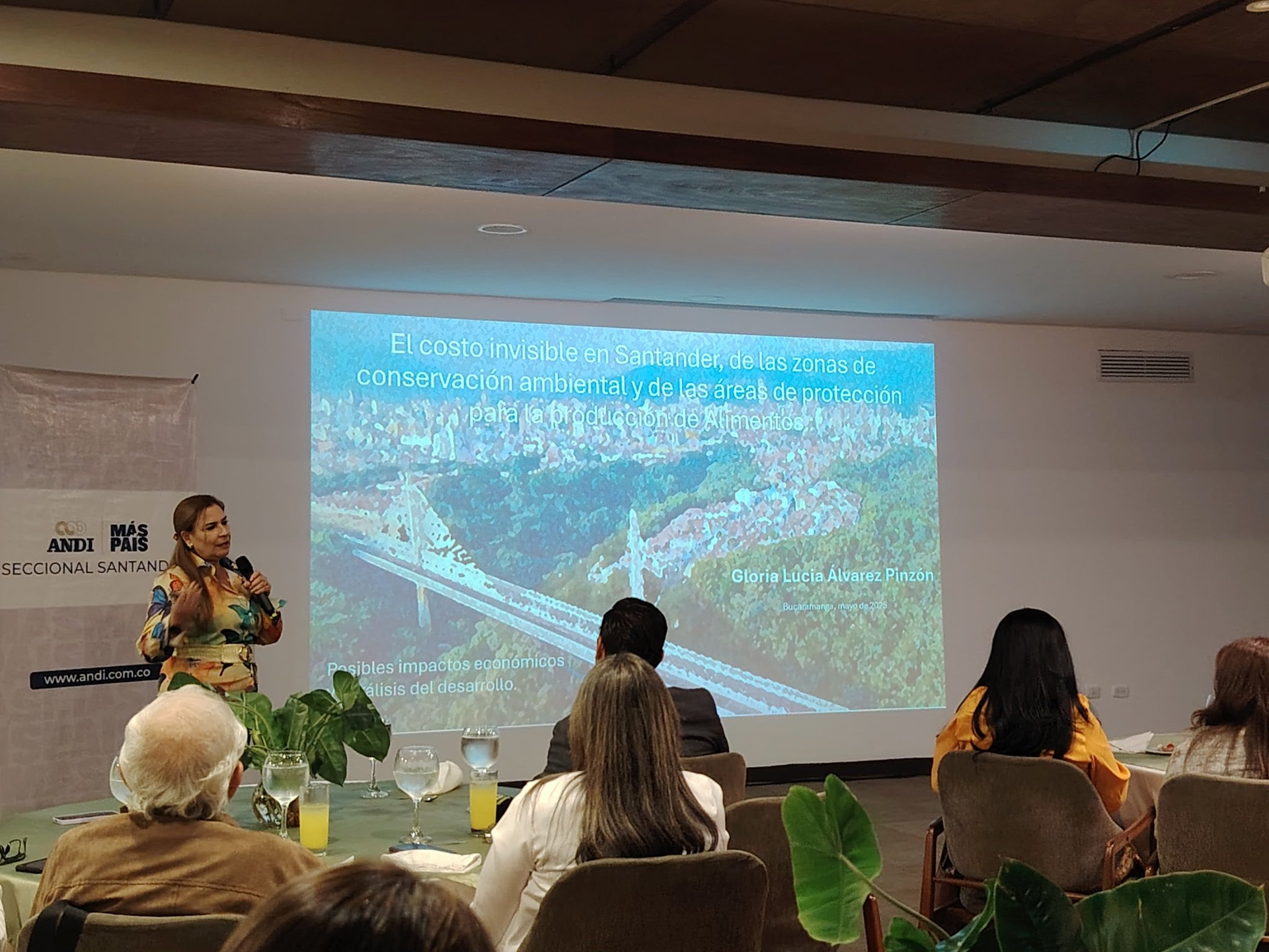 Un orador realiza una presentación ante un público en una sala con una gran pantalla de proyección
