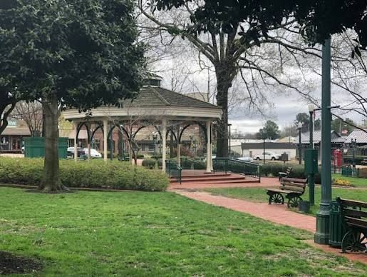 Park gazebo with benches beside a brick path and green lawn under cloudy skies.