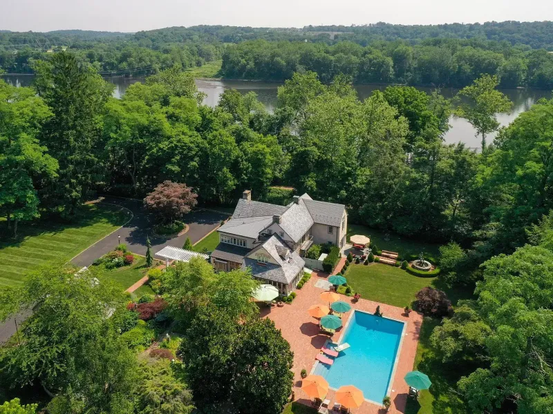 Aerial view of a house with a turquoise pool, patio, and lush green trees surrounding the property.