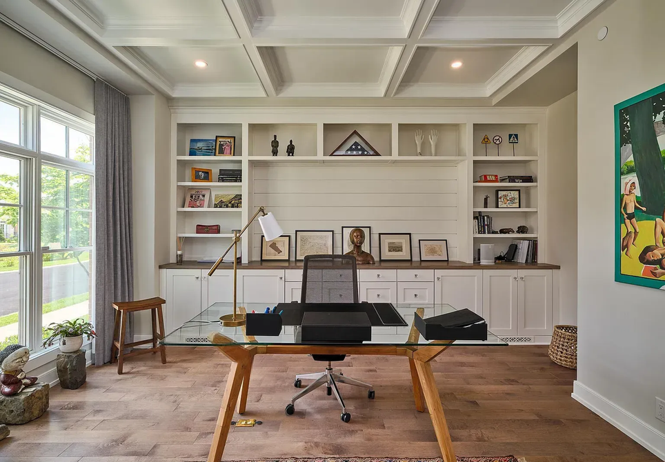 Bright home office with white built-ins, wooden desk, and large windows on the left.