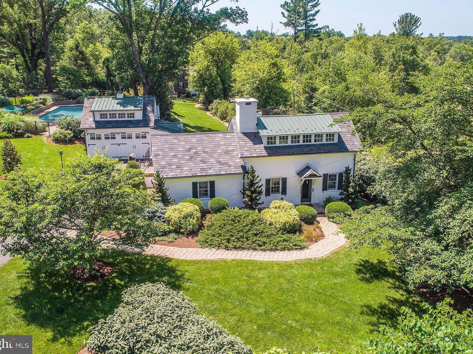 White house with gray roof amid lush green trees and lawn
